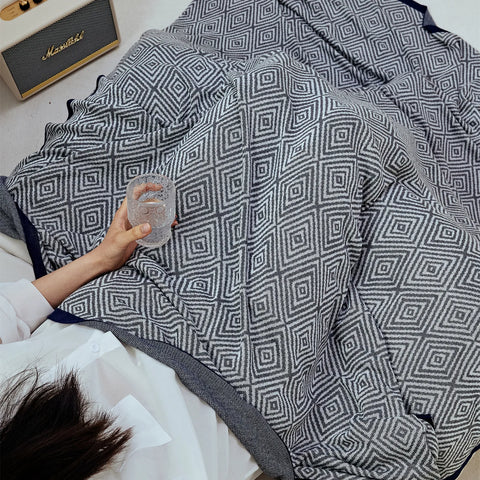 Close-up of a person covered by the charcoal-grey diamond pattern throw, highlighting the dense pattern and dark edge.