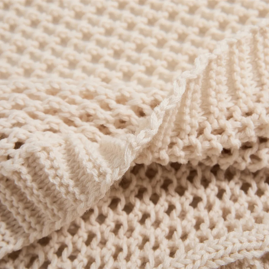 Detailed close-up of the cream-white knit throw's texture, showing the ribbed border and open-knit hole pattern.