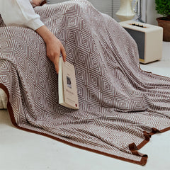 Close-up of a person reading, covered by the dusty-pink diamond pattern throw, highlighting the soft weave and edge.