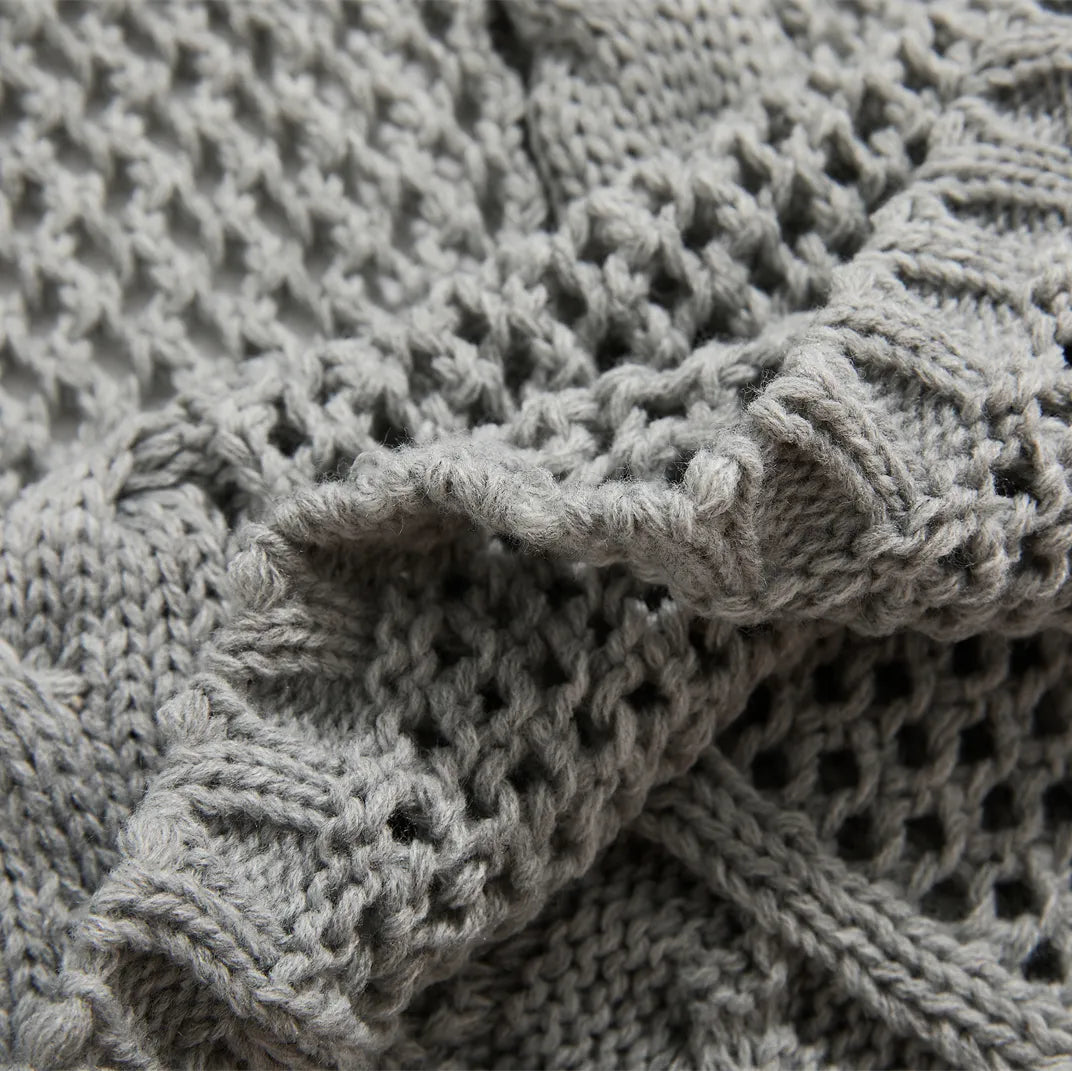 Detailed close-up of the light-grey knit throw's texture, showing the cable-knit and open-knit mesh sections.