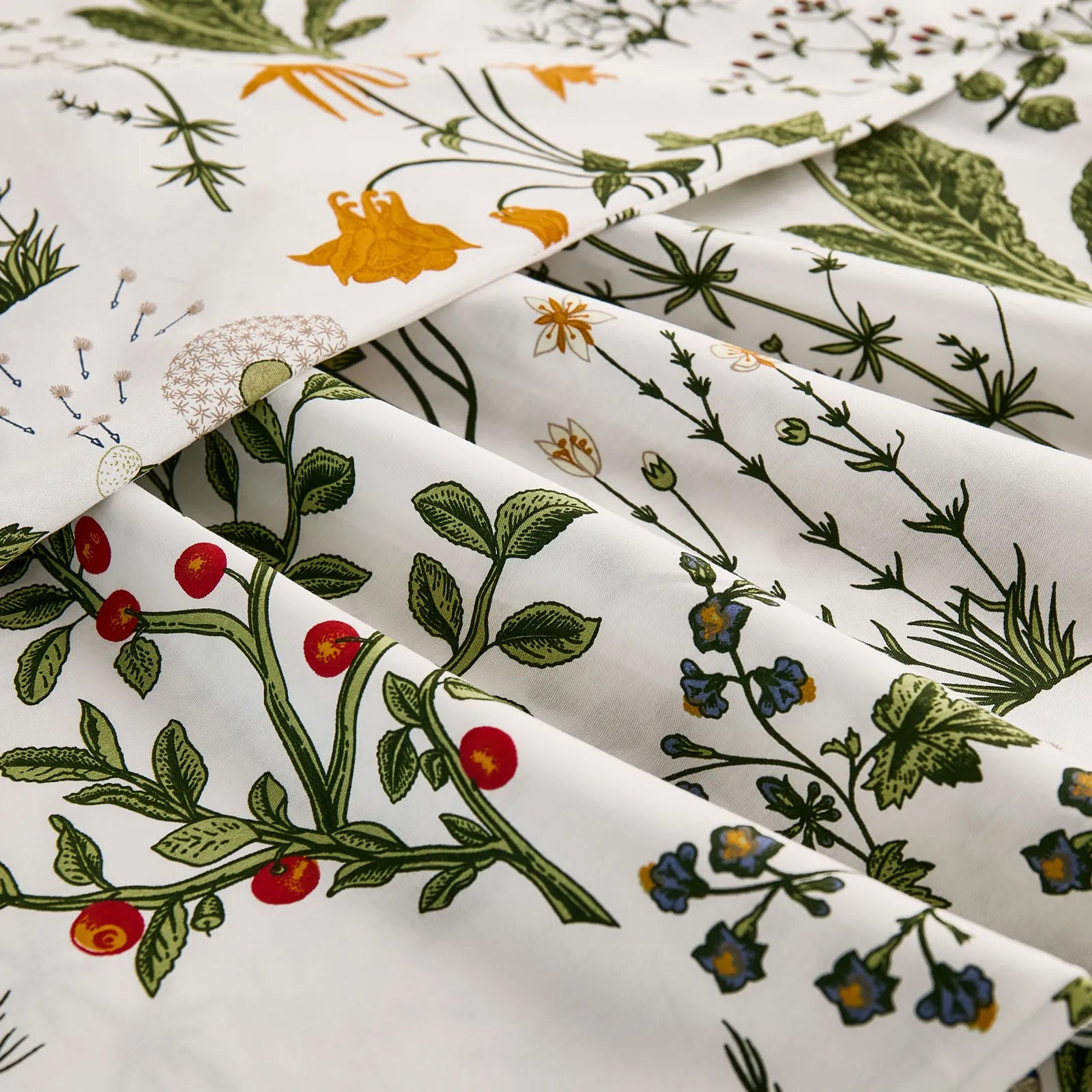A close-up of the folded white cotton fabric, showcasing the intricate botanical print with red berries, yellow flowers, and detailed leaves.