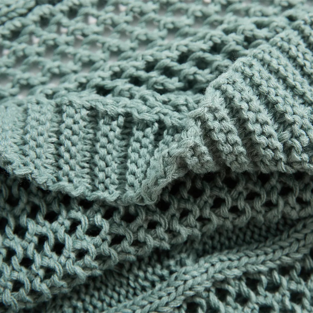Detailed close-up of the sage-green knit throw's texture, showing the cable-knit, open-knit, and ribbed sections.
