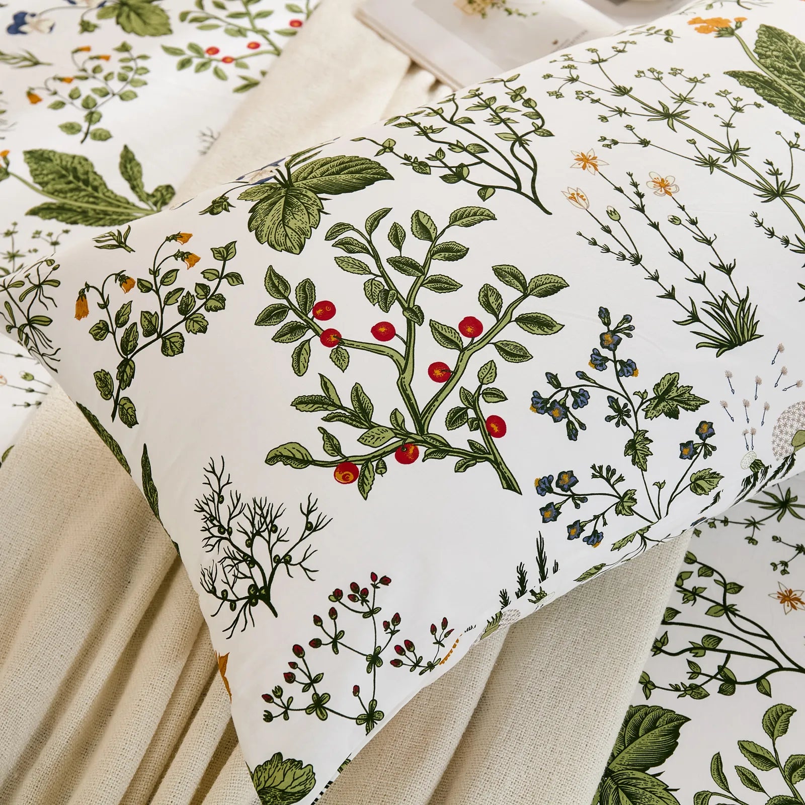 A close-up view of a white cotton pillowcase, highlighting the detailed botanical pattern with red berries, leaves, and various small flowers.