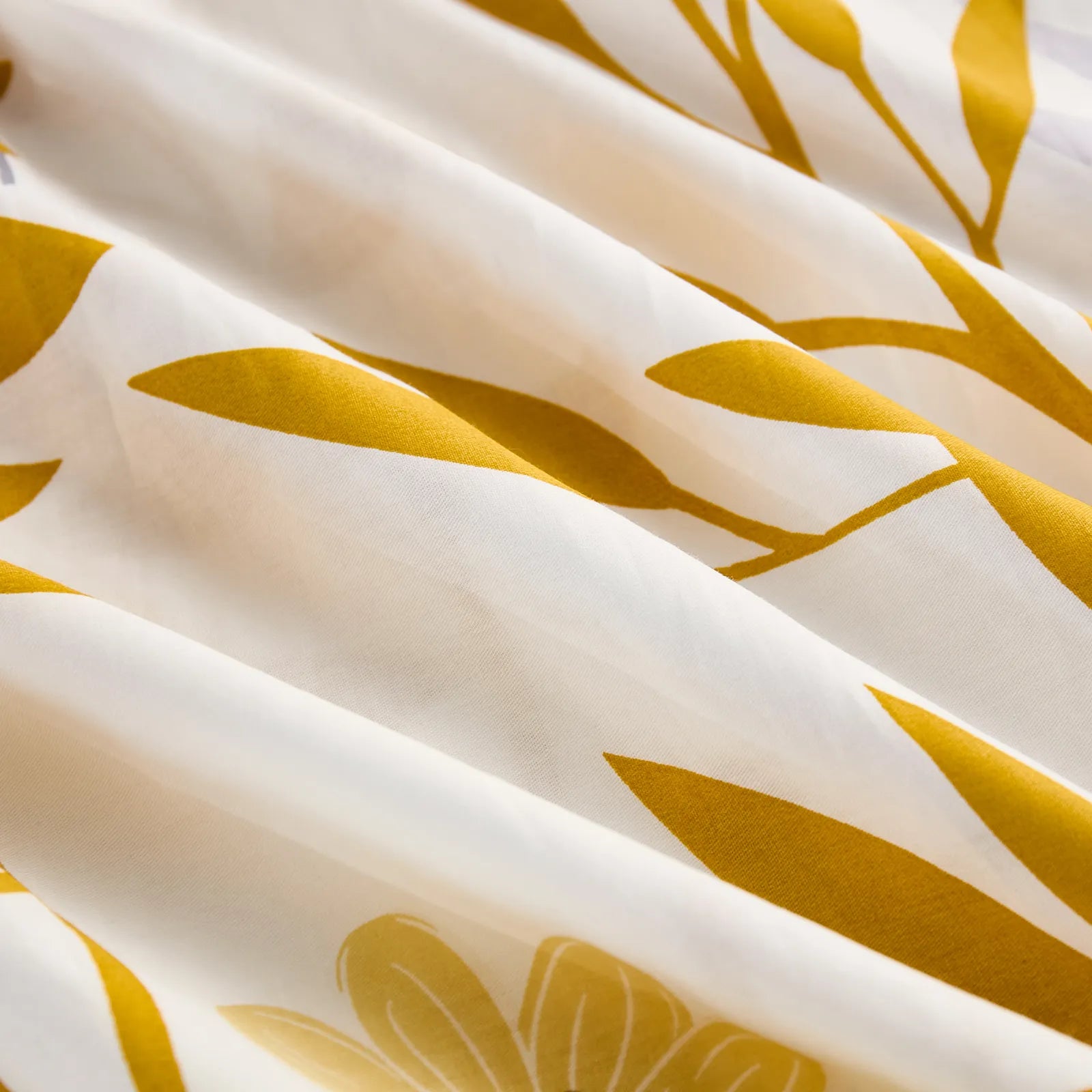 A close-up shot of the folded white cotton fabric, emphasizing the detailed print of bright yellow leaves and subtle flowers.