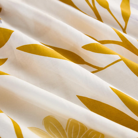 A close-up shot of the folded white cotton fabric, emphasizing the detailed print of bright yellow leaves and subtle flowers.