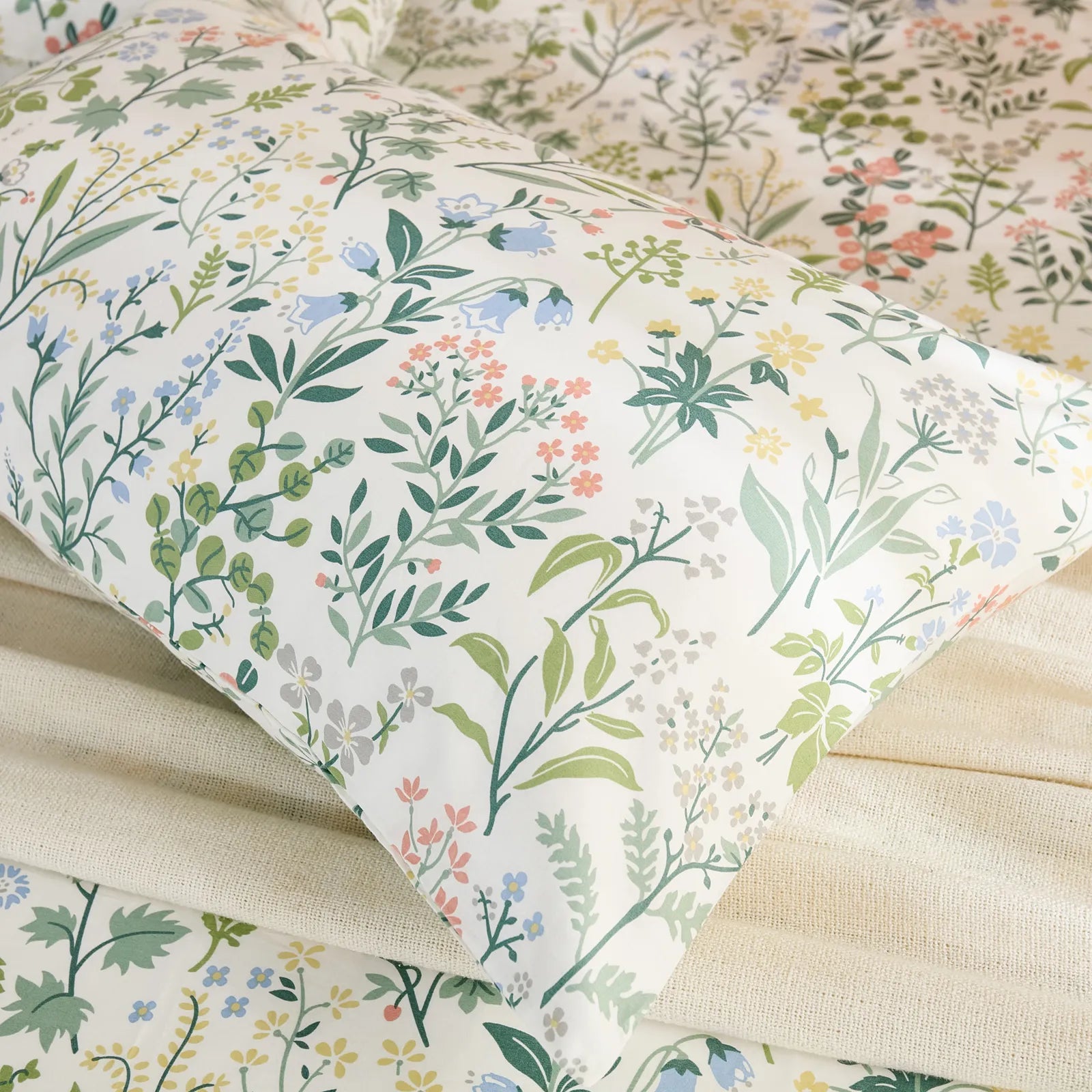 A close-up, angled view of a cotton floral pillowcase, highlighting the detailed botanical pattern with various leaves and flowers in soft pastel colors.