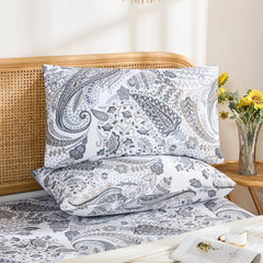  A flat-lay photo of two cotton grey paisley pillow shams and a matching sheet, shown on a white quilted duvet with small accent pillows.