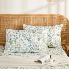 Two cotton meadow flower pillowcases are neatly arranged on a bed with a rattan headboard, styled with a book and a teacup.