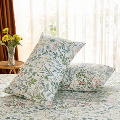 A pair of cotton meadow print pillowcases are propped on a bed, with a sunlit window and yellow sunflowers providing a warm, natural backdrop.