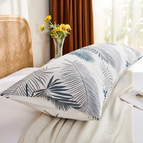 A side-angled view of a tropical palm leaf cotton body pillowcase on a bed, showing the end of the pillowcase and the woven rattan headboard.