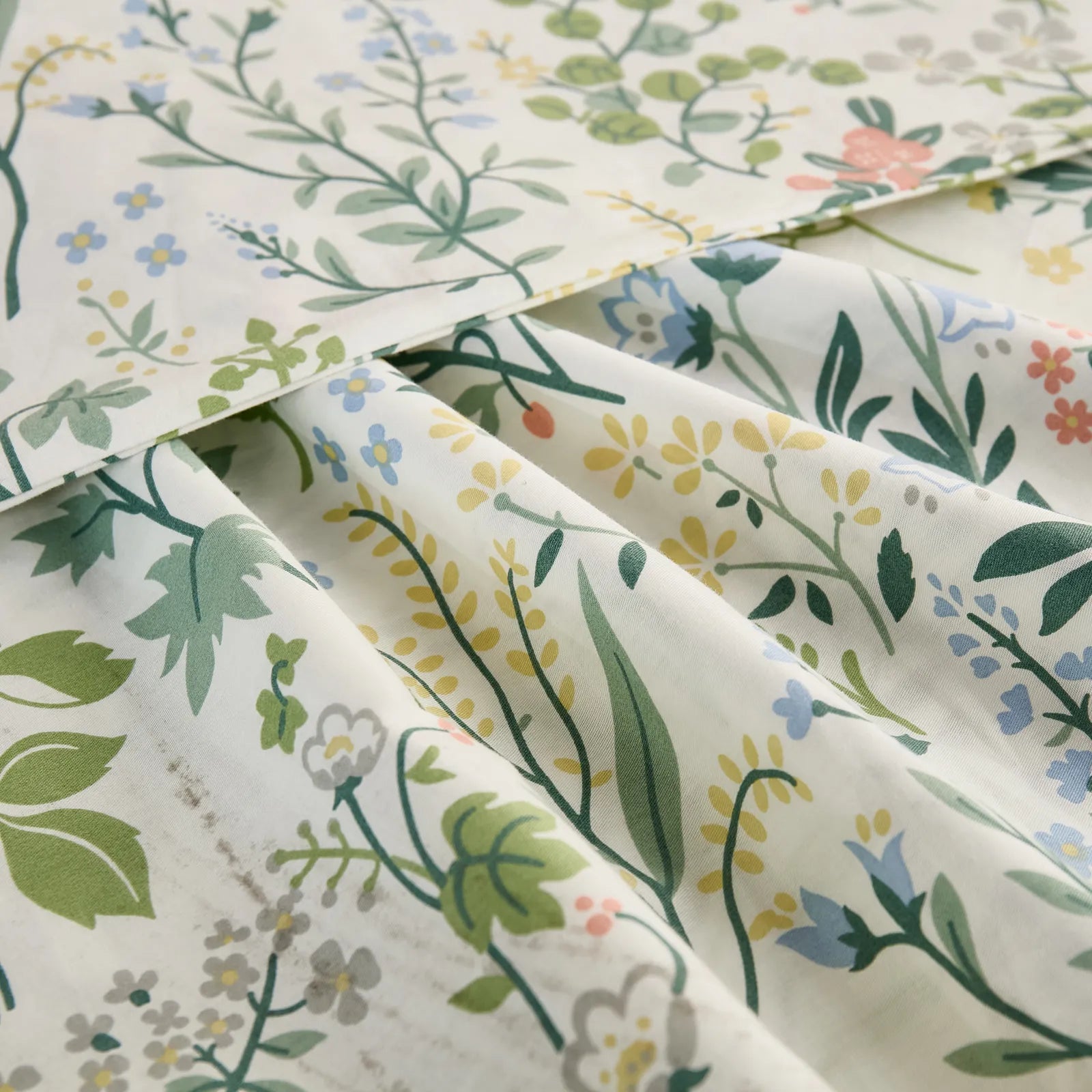 A close-up shot of the cotton fabric, showing the intricate folds and the detailed wildflower pattern in soft green, blue, and pink tones.
