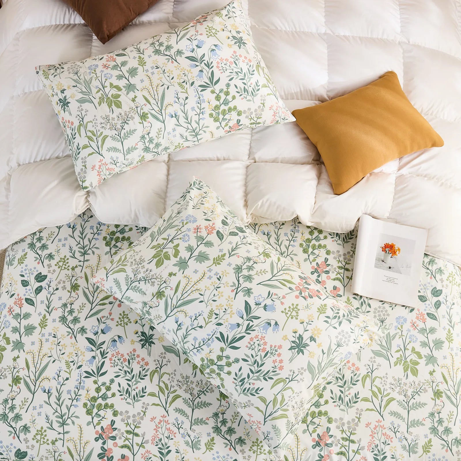 An overhead flat-lay shot of two cotton wildflower print pillowcases and a matching sheet on a white quilted duvet with brown and mustard pillows.