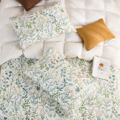 An overhead flat-lay shot of two cotton wildflower print pillowcases and a matching sheet on a white quilted duvet with brown and mustard pillows.