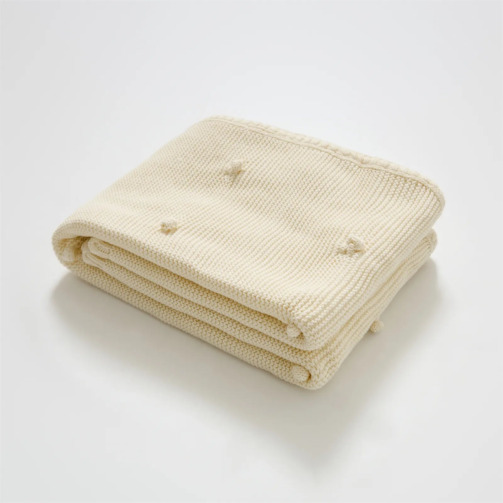 Neatly folded cream white cotton knit throw blanket with fringe trim and bobble texture