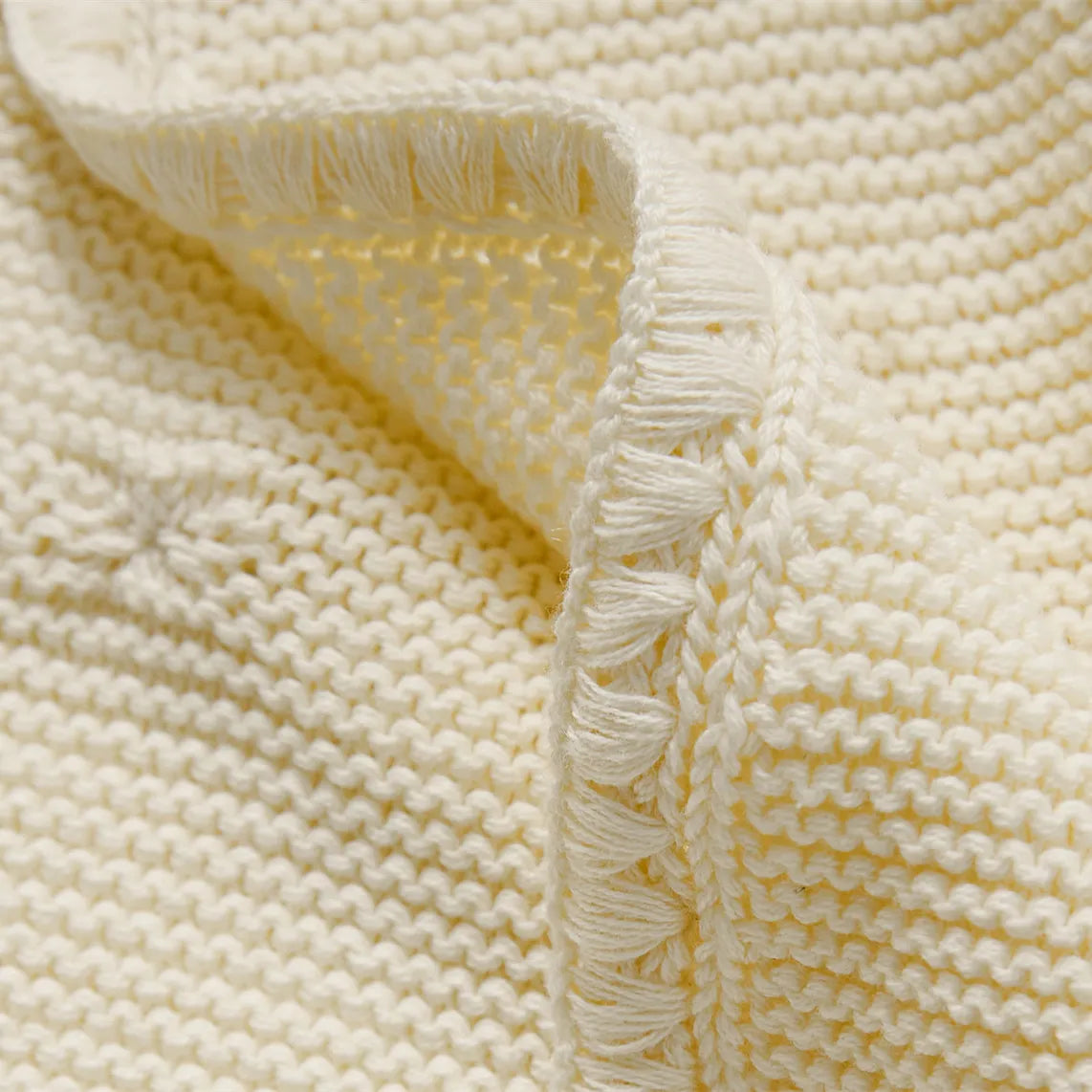 Close up detail of cream white cotton knit fabric and the decorative fringe border