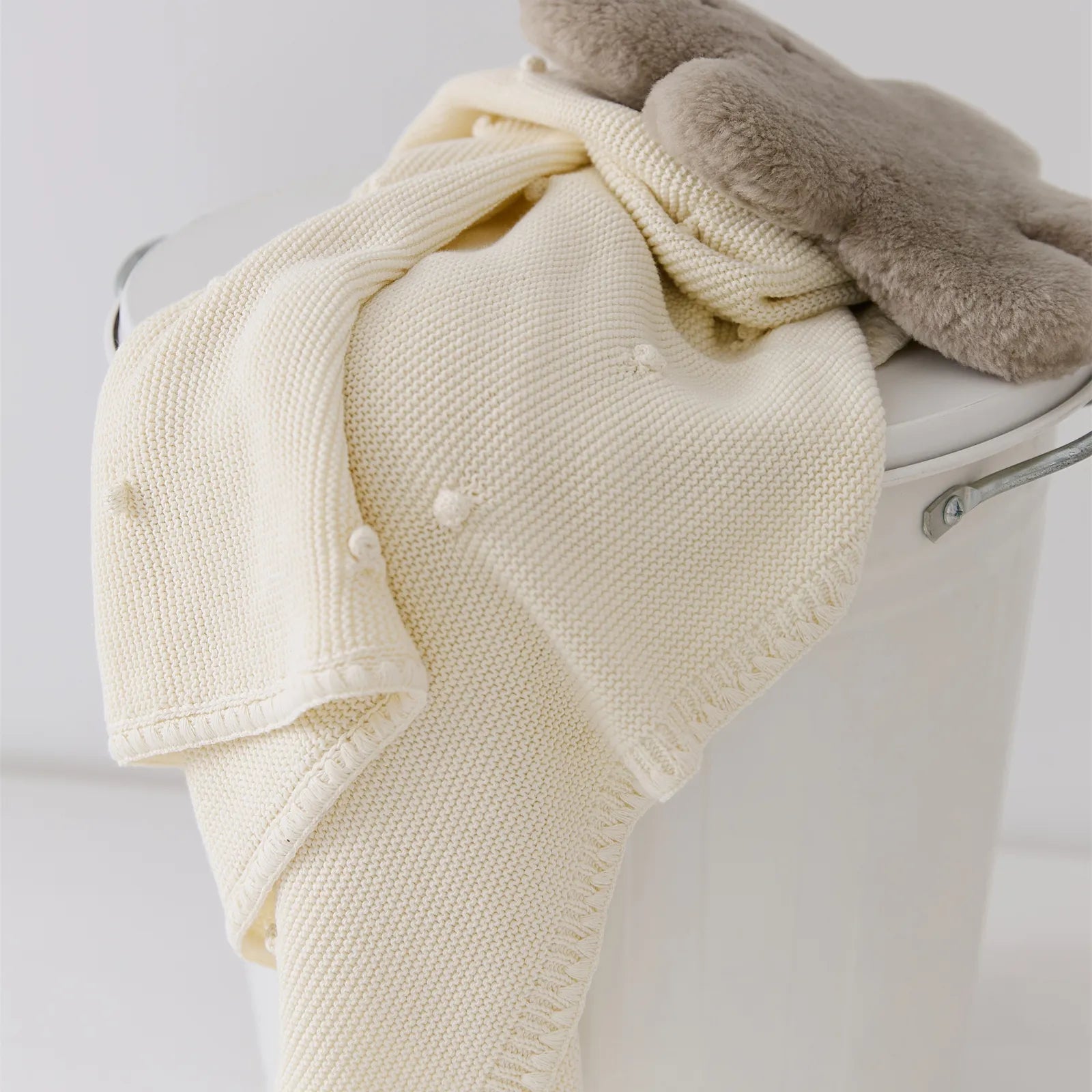 Cream white cotton bobble throw draped over a white storage bucket with a soft plush toy