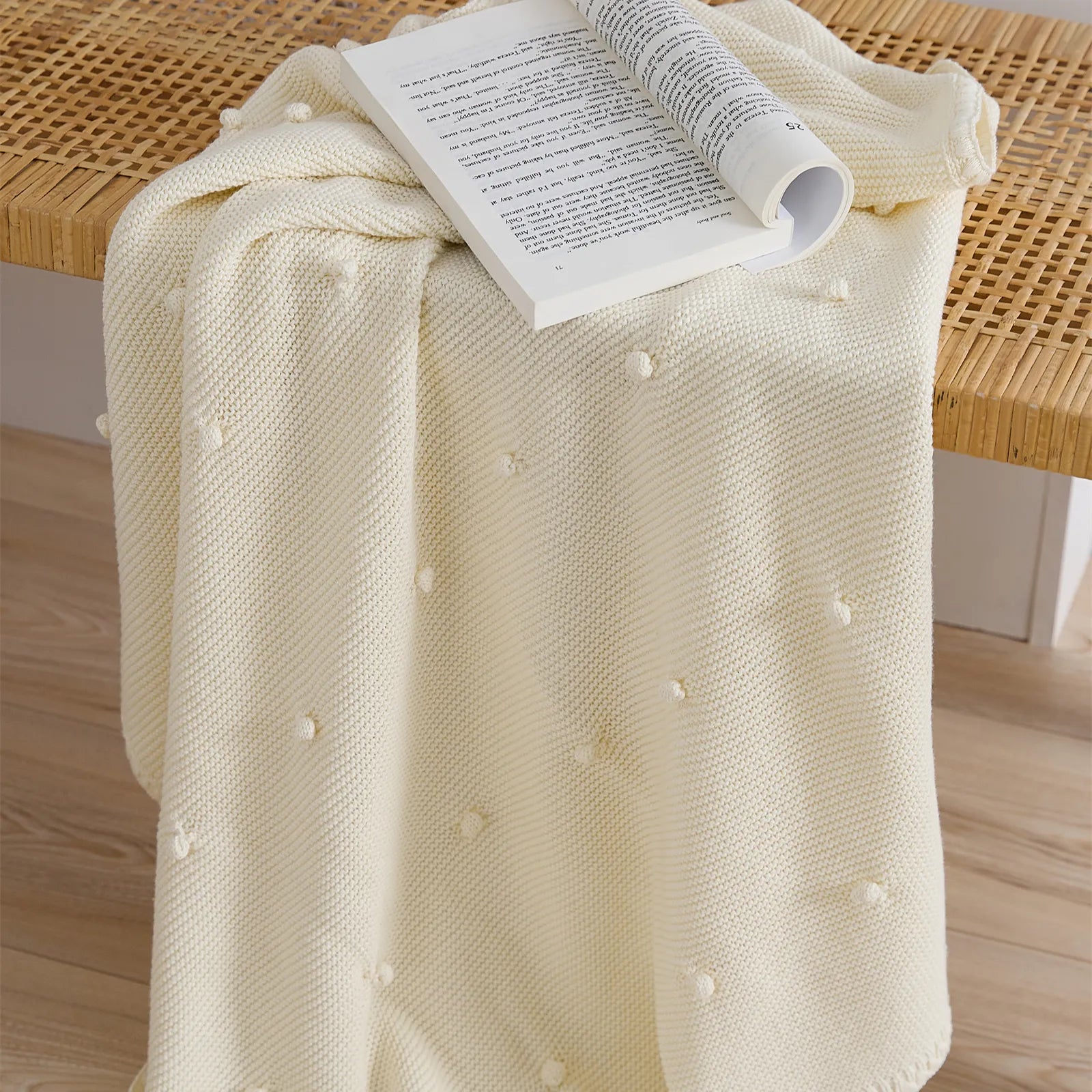 Cream white cotton bobble throw draped over a rattan woven bench with an open book
