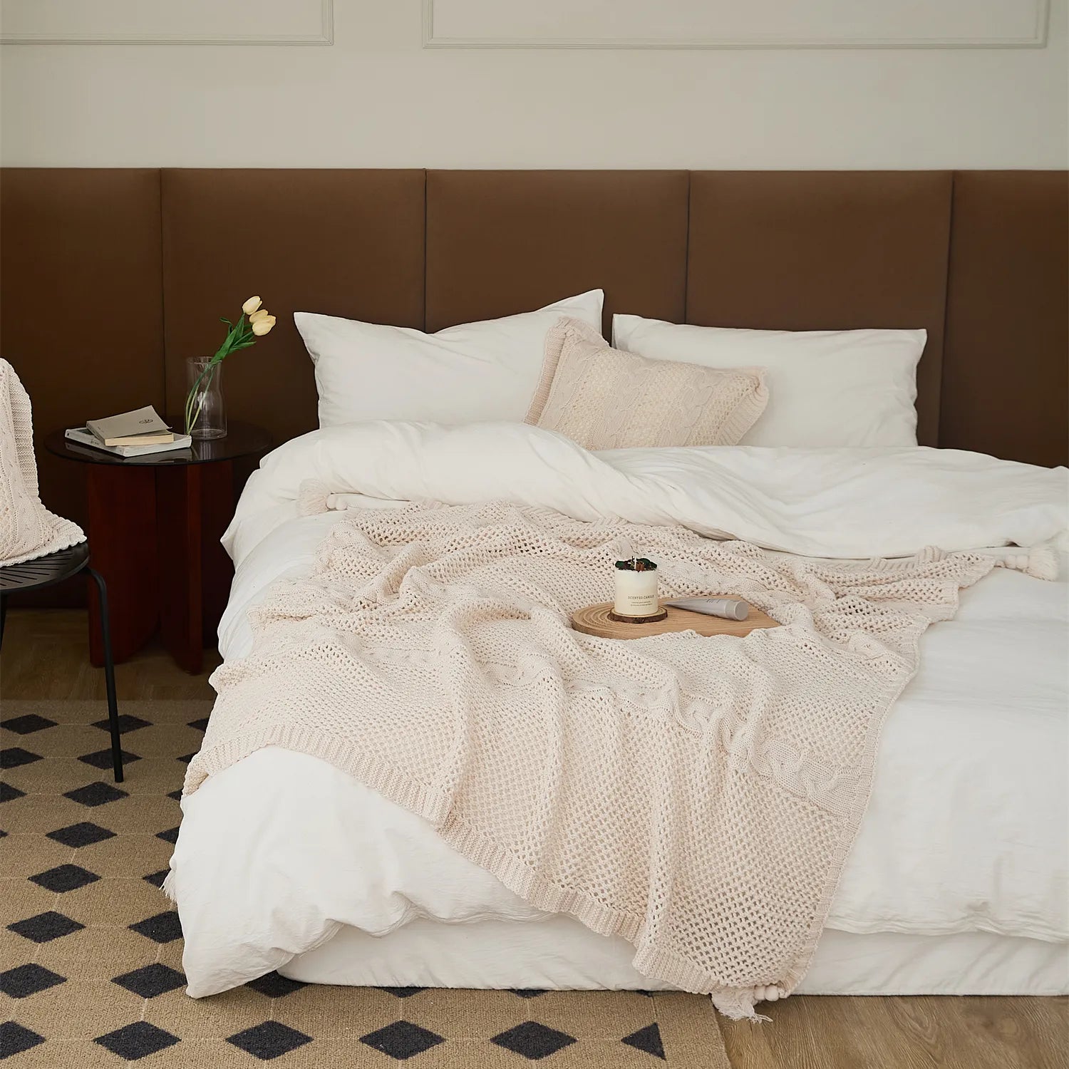 Cream-white knit throw blanket with cable stripes and tassels casually draped on a white bed.