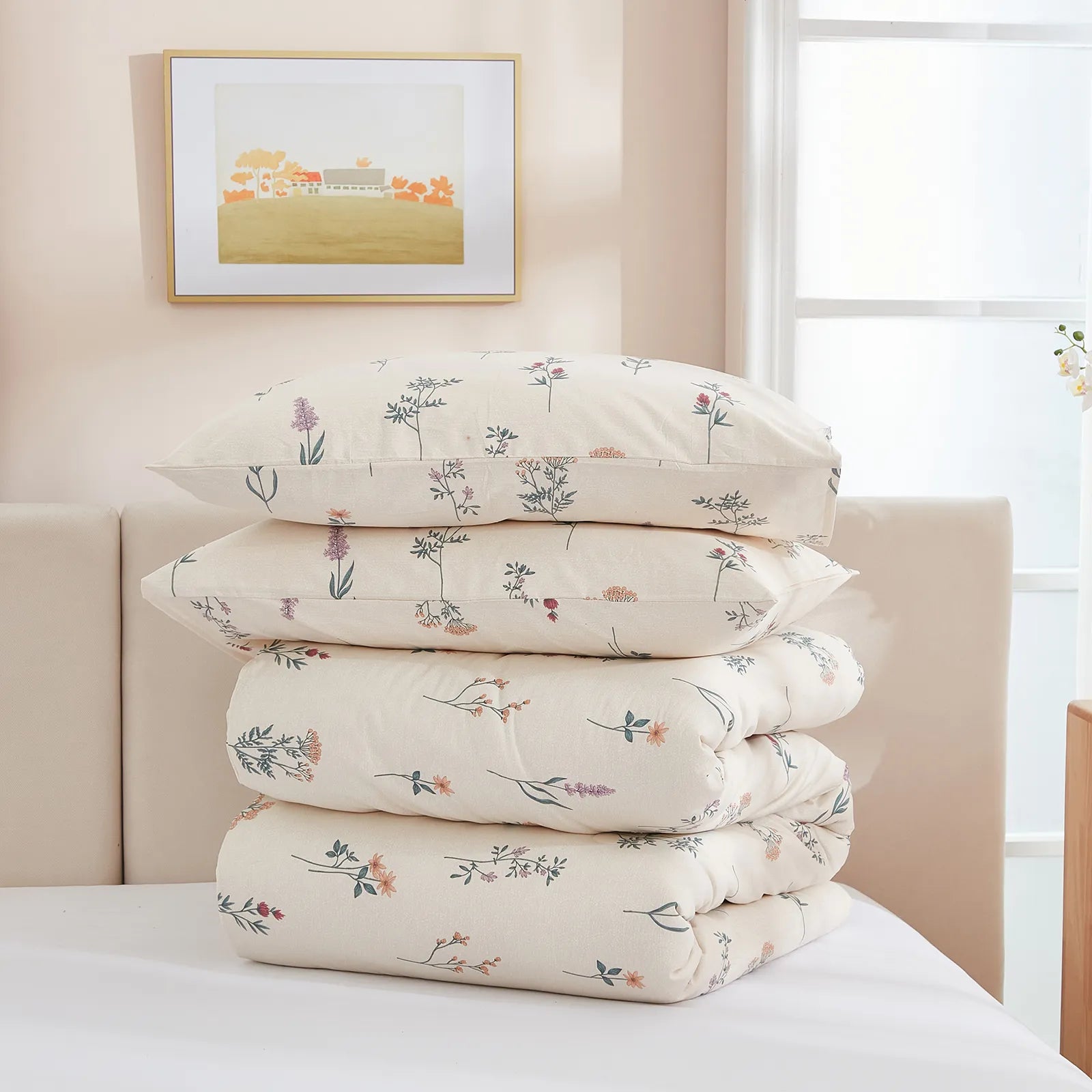 A stack of two floral pillowcases and a folded comforter on a bed against a neutral headboard.