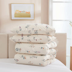 A stack of two floral pillowcases and a folded comforter on a bed against a neutral headboard.