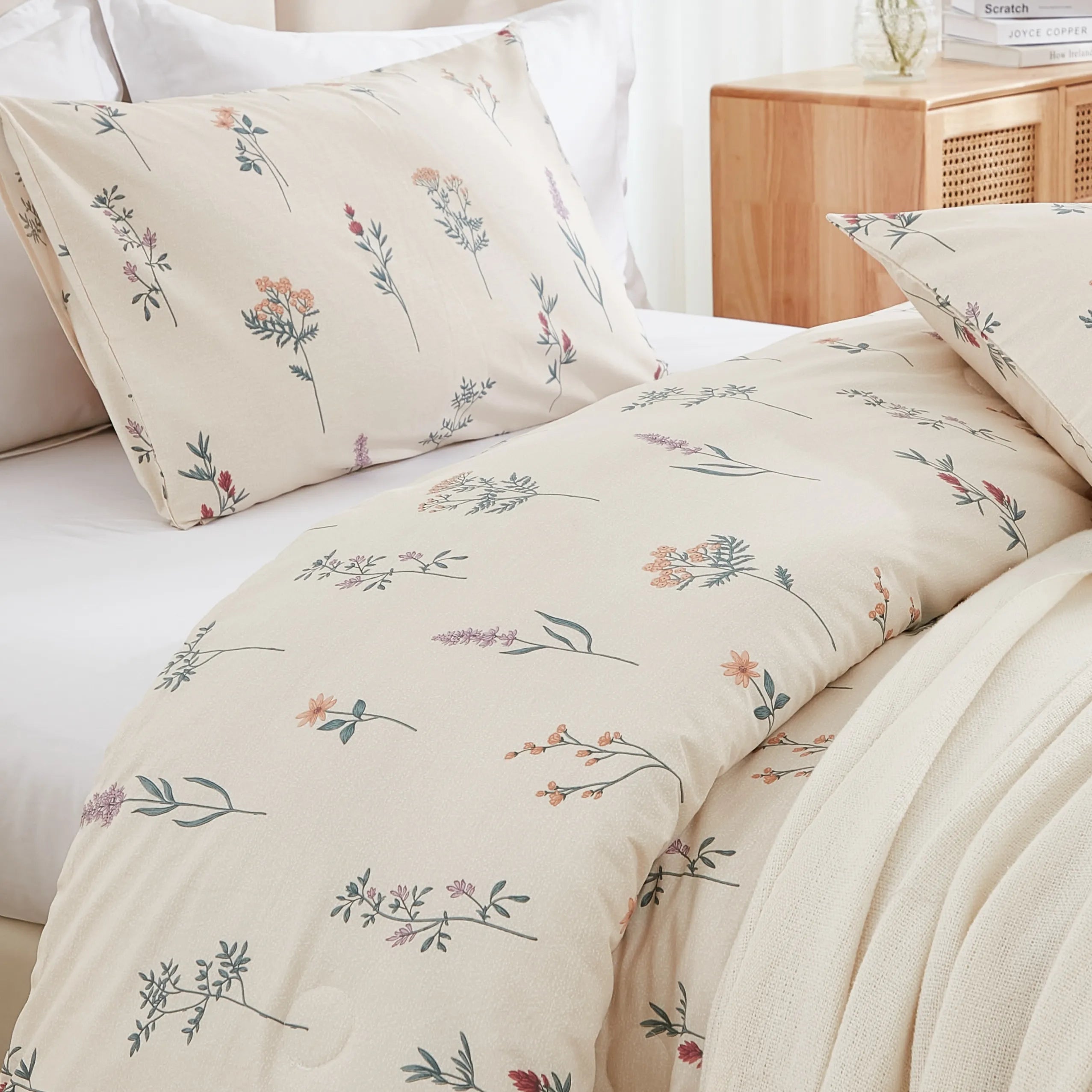 Detailed view of a bed with a floral comforter, beige blanket, and a festive garland hanging over the headboard.