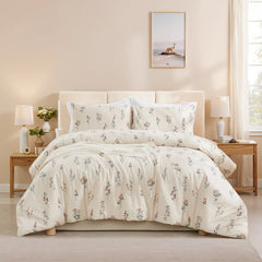 Full view of a bed with a cream-colored floral comforter set, two lamps, and a framed picture on the wall.