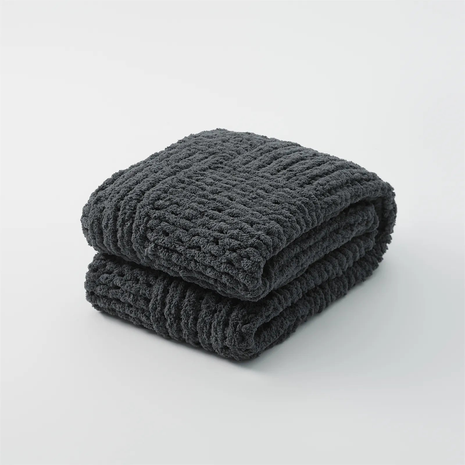 A studio shot of a perfectly folded dark gray chunky knit blanket, highlighting its deep color and woven texture.