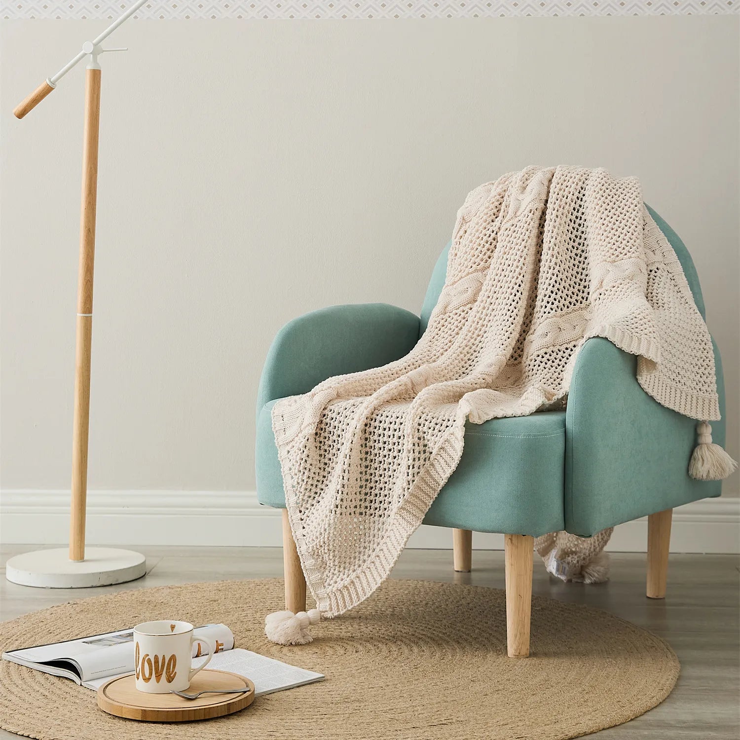 Cream-white knit throw with tassels draped over a teal armchair, in a cozy living room setting.