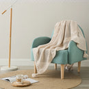 Cream-white knit throw with tassels draped over a teal armchair, in a cozy living room setting.