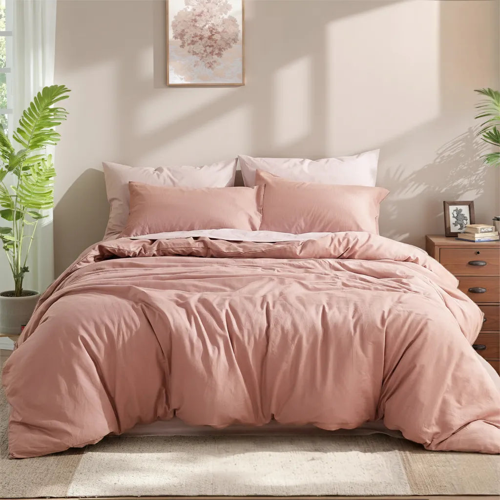 Front view of a dusty pink cotton duvet with layered pillows, under a pink floral art piece on a light wall.