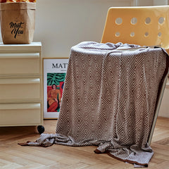 Dusty-pink diamond pattern throw draped over a modern yellow chair in a bright indoor setting.
