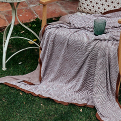 Dusty-pink diamond pattern throw draped over a wooden chair outdoors on the grass, next to a small side table.