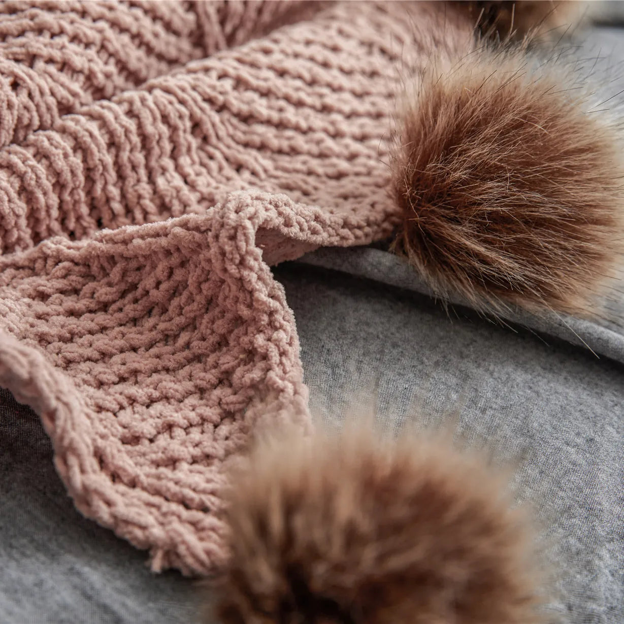 Detail of soft dusty pink knit fabric with large brown faux fur pom-pom on grey background