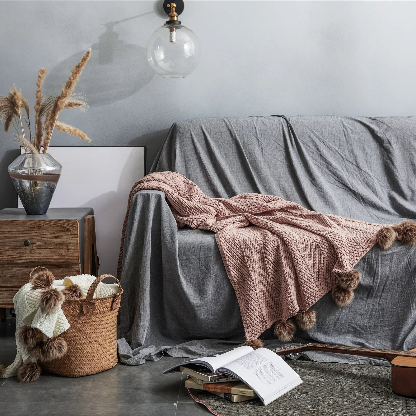 Dusty pink pom-pom throw draped on grey sofa in cozy living room setup