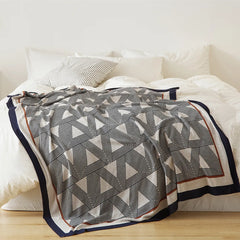 full view of the geometric throw blanket on a white bed, showing its striking pattern and elegant border.