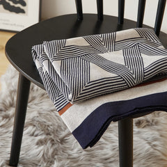 A modern geometric knit blanket with a black, white, and brown pattern, neatly folded on a black chair.
