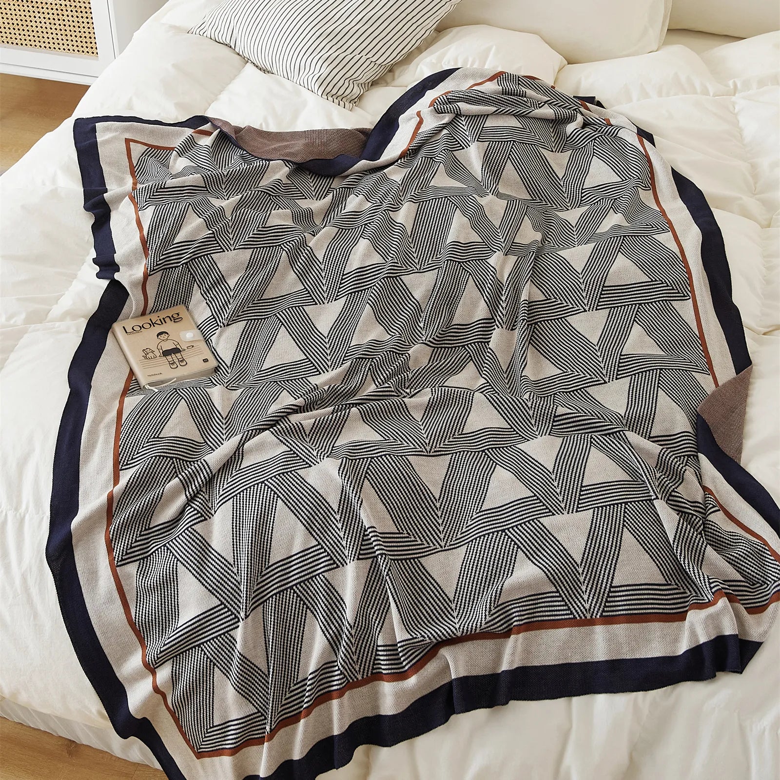 A modern geometric throw blanket with a triangle pattern and a striped border, styled on a white bed.