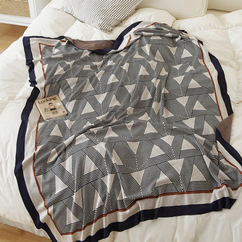 A modern geometric throw blanket with a triangle pattern and a striped border, styled on a white bed.