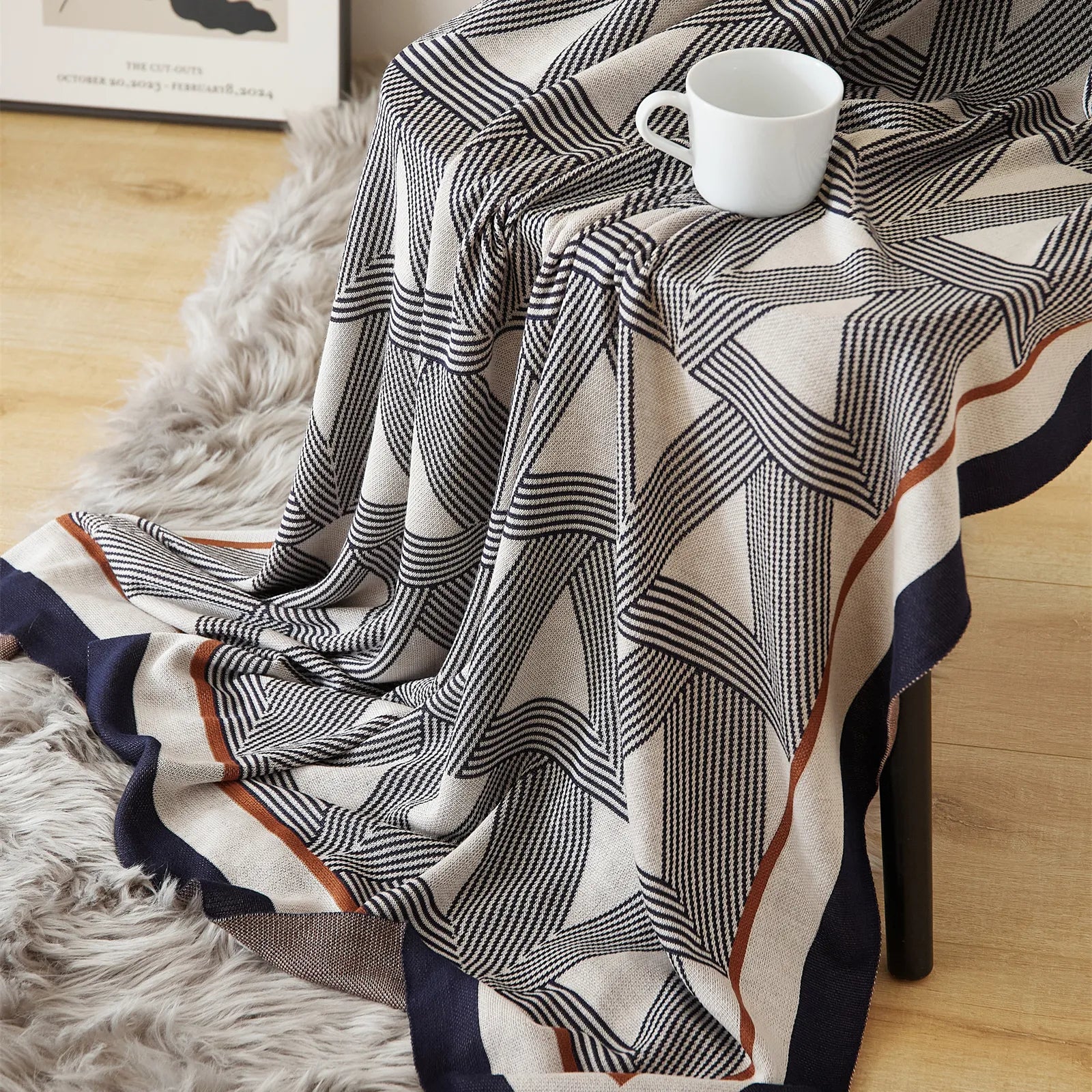 A stylish geometric knit blanket with a cup on a chair, showcasing its unique triangle design and warm tones