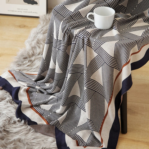 A stylish geometric knit blanket with a cup on a chair, showcasing its unique triangle design and warm tones