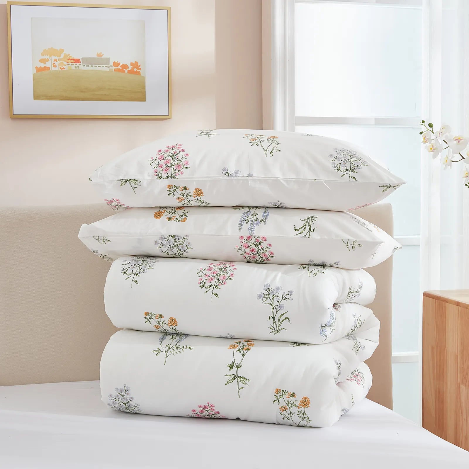 A stack of two pillows and a folded comforter from a floral duvet set on a white bed.