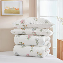 A stack of two pillows and a folded comforter from a floral duvet set on a white bed.