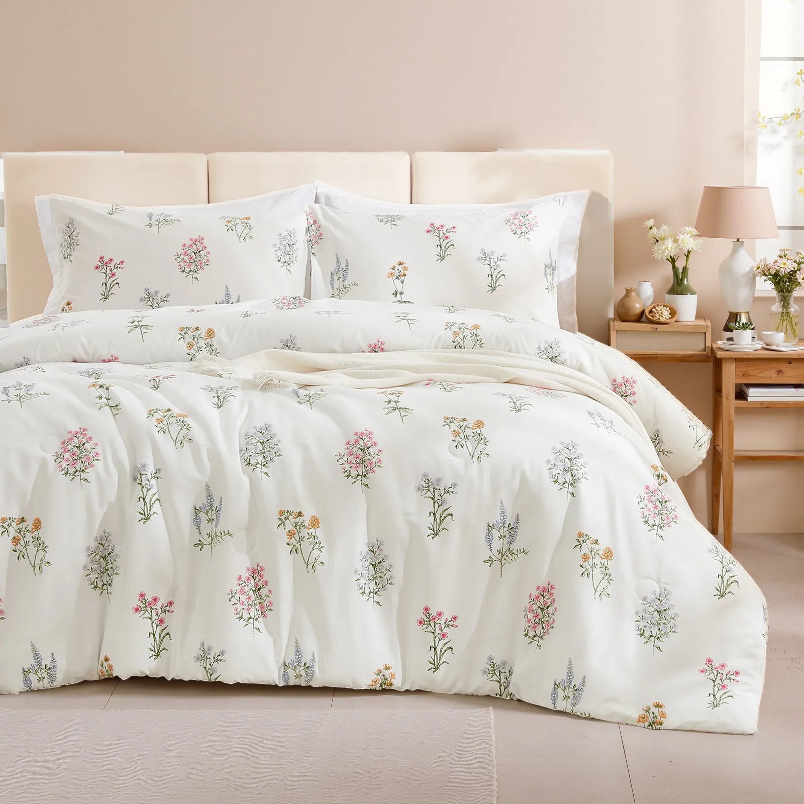 A styled bed with a white comforter set featuring small, multicolored floral bouquets and a beige knit blanket