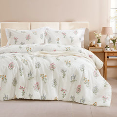 A styled bed with a white comforter set featuring small, multicolored floral bouquets and a beige knit blanket
