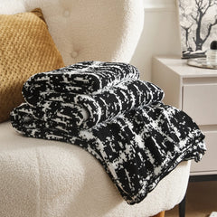 A close-up shot of the folded black and white artistic wool blanket, showcasing its unique pattern and soft texture on an armchair.