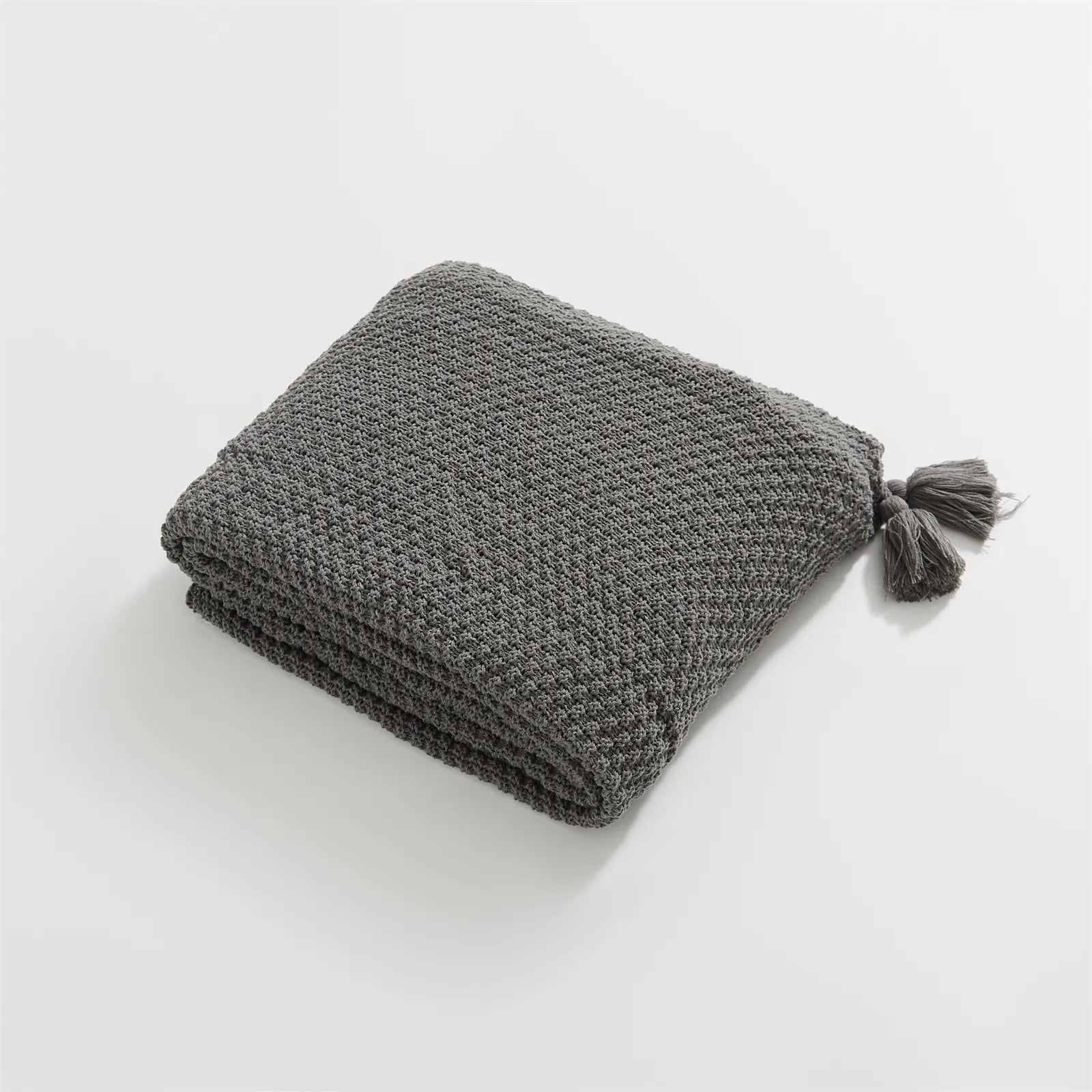 Folded Charcoal Knitted Throw Blanket Showing Tassel on White Background