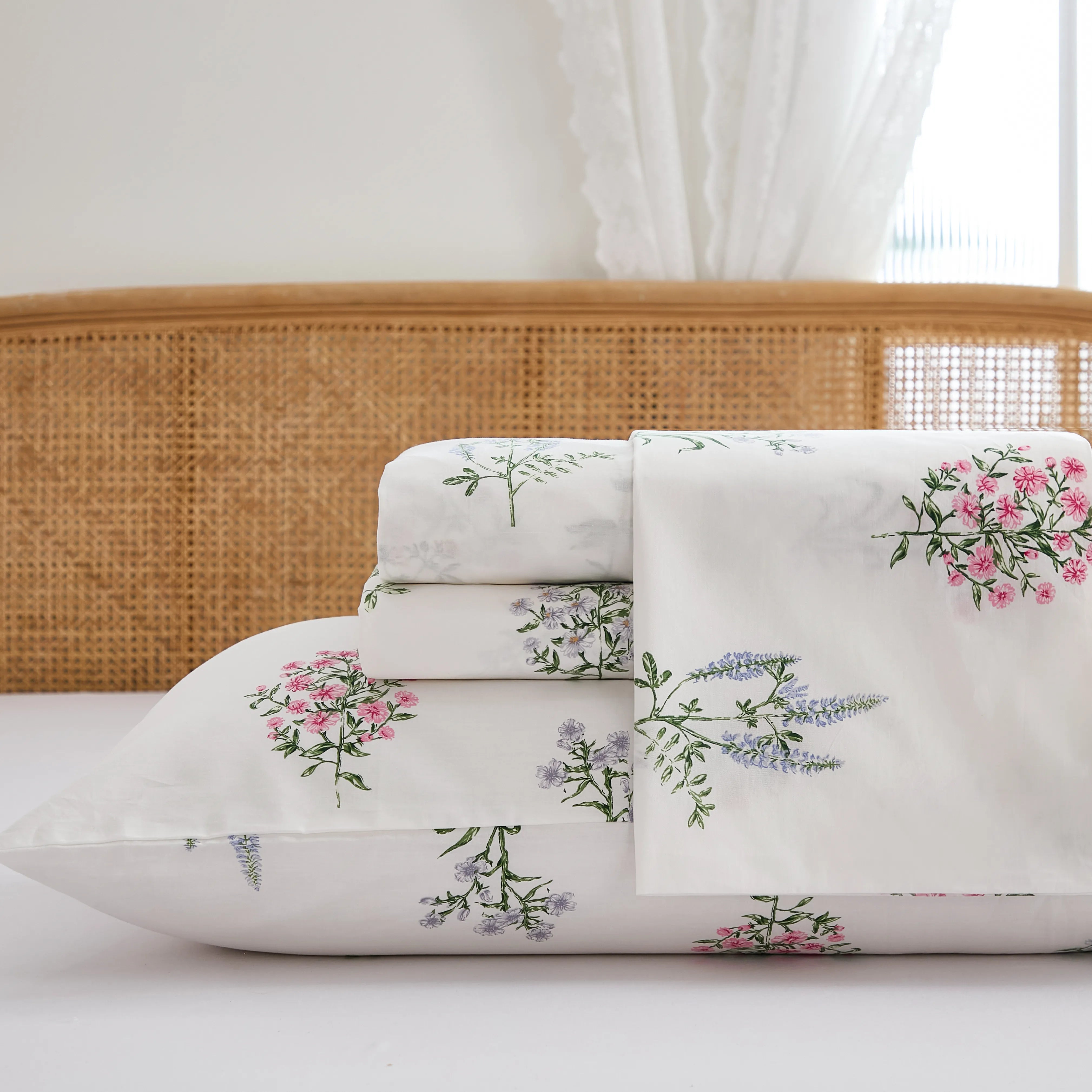 Close up stack of folded cotton wildflower fitted sheet and pillowcases on white