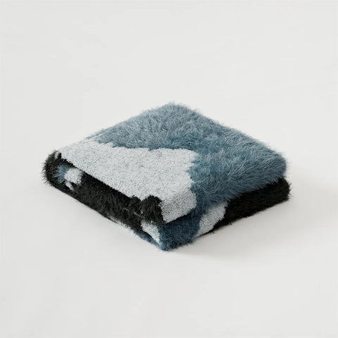 Neatly folded abstract fuzzy knit throw blanket in teal and black studio shot