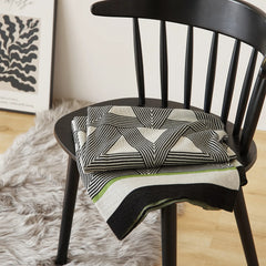 A neatly folded geometric throw blanket with green and black borders sits on a modern black chair.