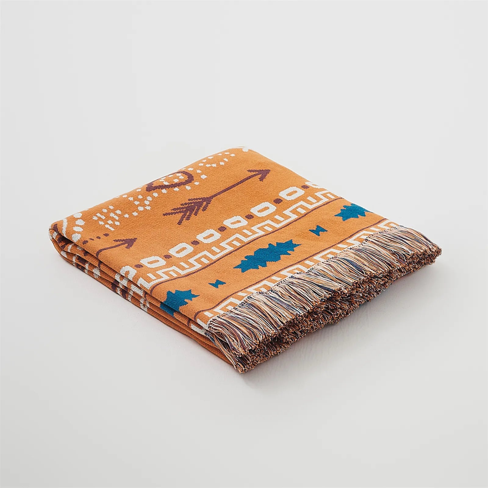 Folded orange bohemian jacquard cotton throw blanket with fringes, studio shot.